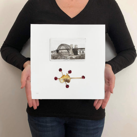 Person holding a framed artwork with a bridge and decorative object on a white background