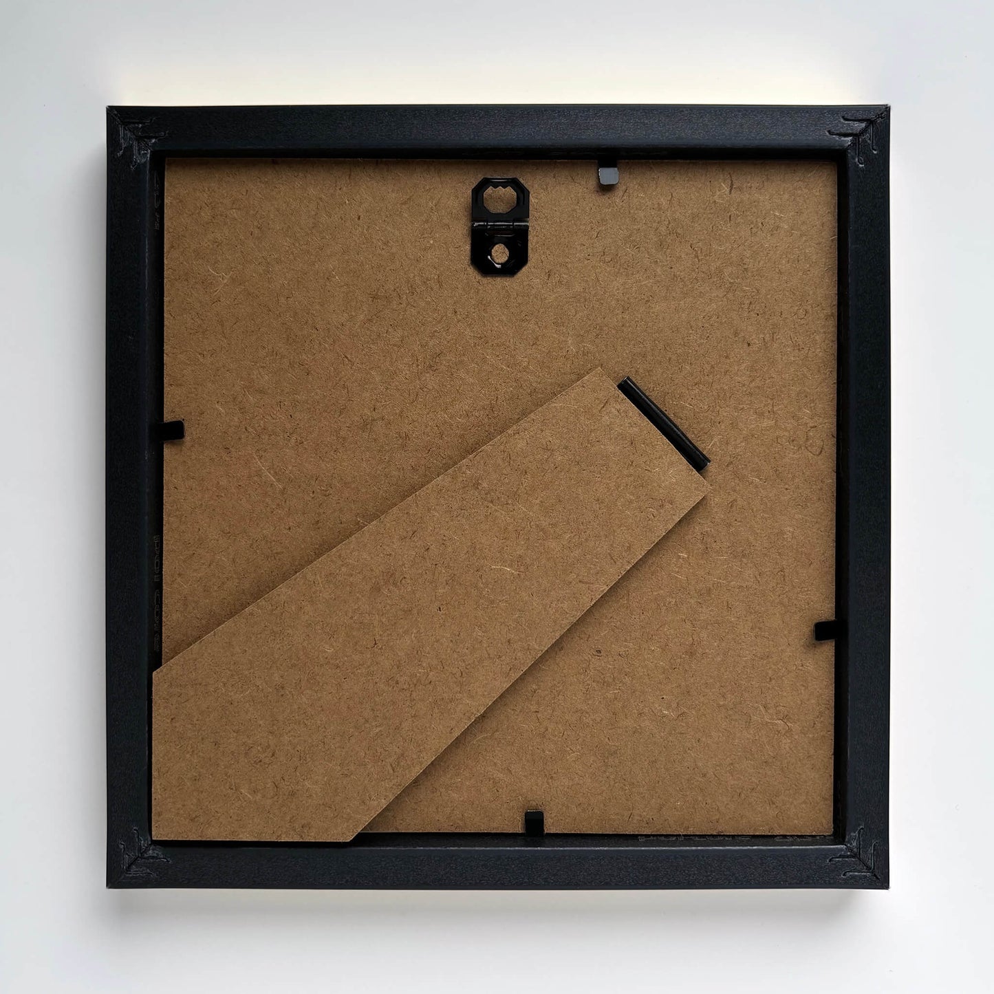 Back of a black picture frame with brown MDF backing on a white background