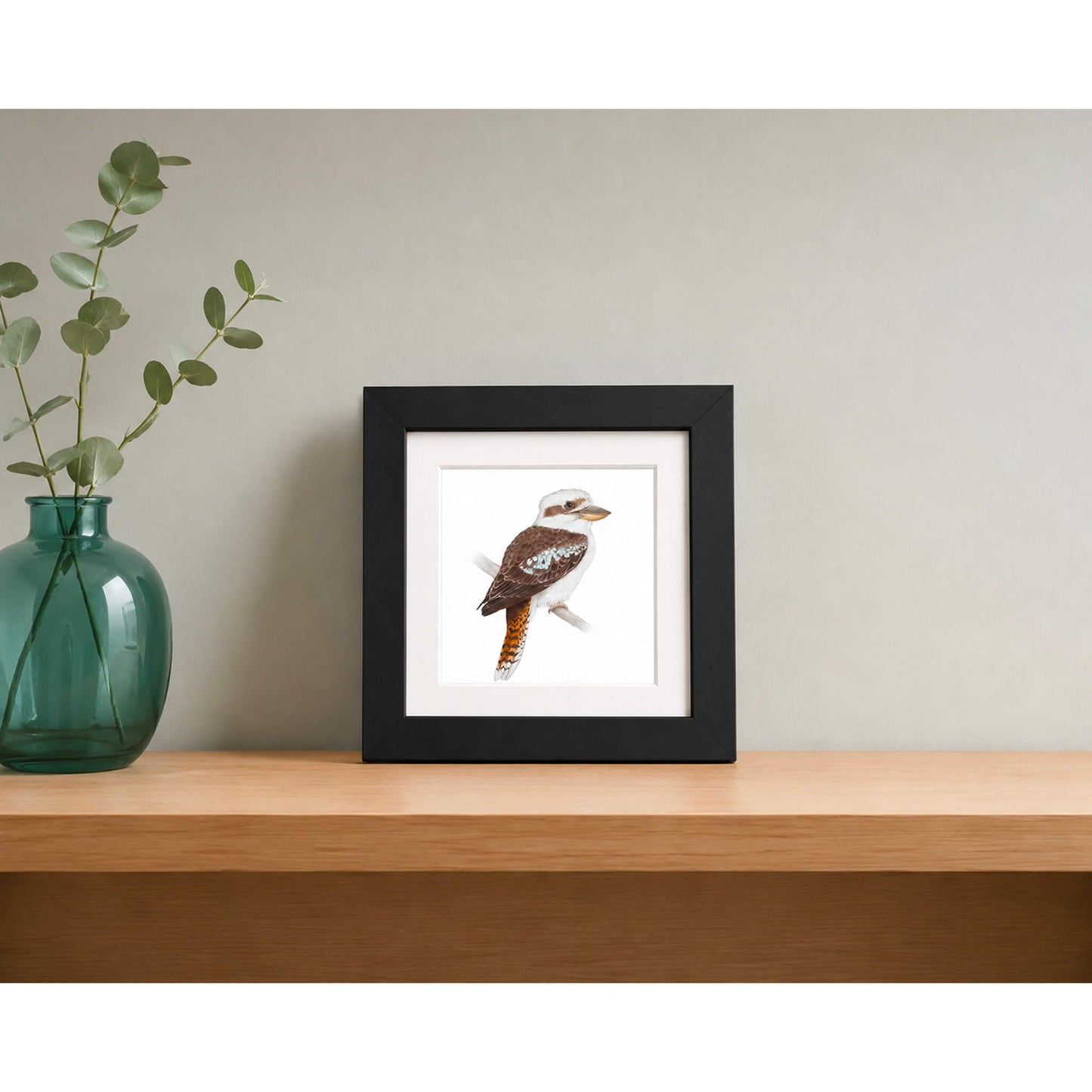 Framed print of a kookaburra on wooden shelf with green glass vase with eucalypt leaves