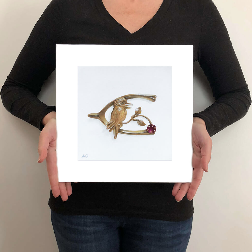 A giclée fine art print of an antique gold and ruby kookaburra pin on a light stone background. This image illustrates the print size.