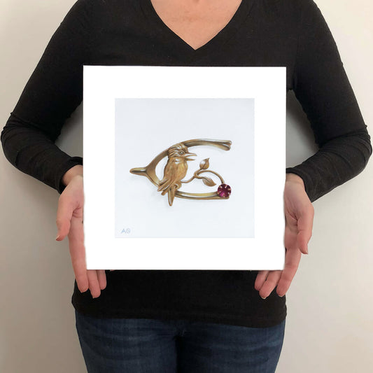 A giclée fine art print of an antique gold and ruby kookaburra pin on a light stone background. This image illustrates the print size.