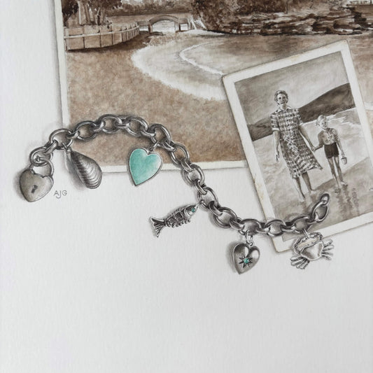 Silver charm bracelet with heart and sea shell charms on a white surface with vintage photos in the background