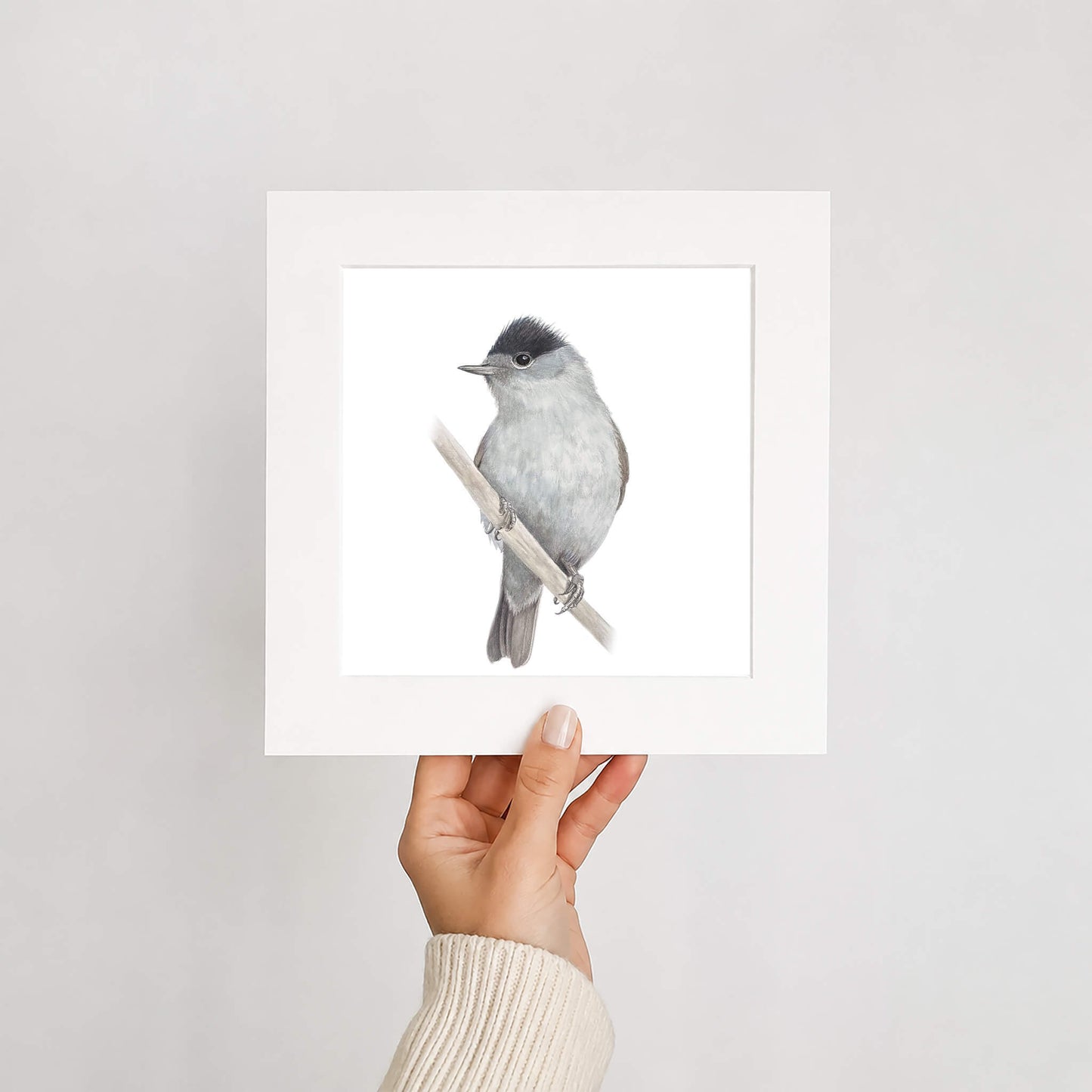 Hand holding a framed print of a bird on a branch against a plain background