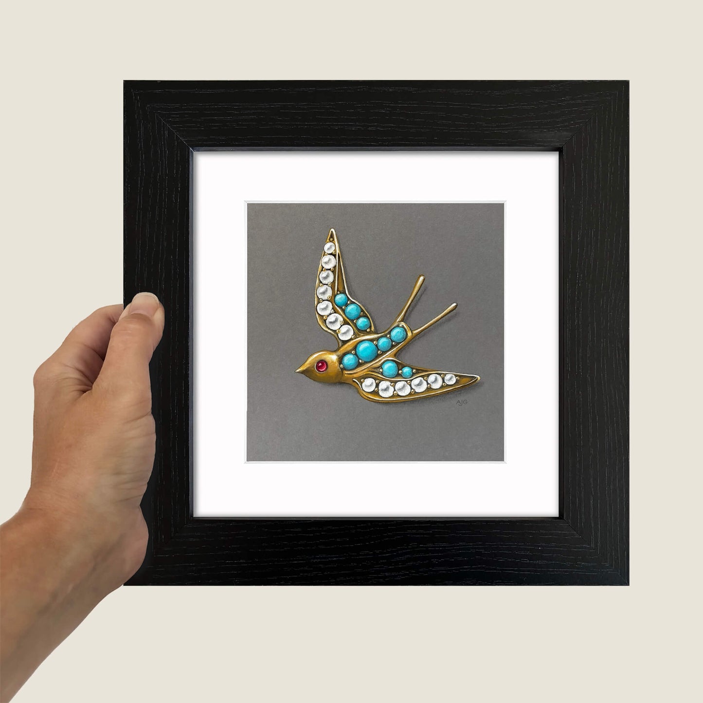 Hand holding a framed painting of a bird brooch with gemstones on a neutral background