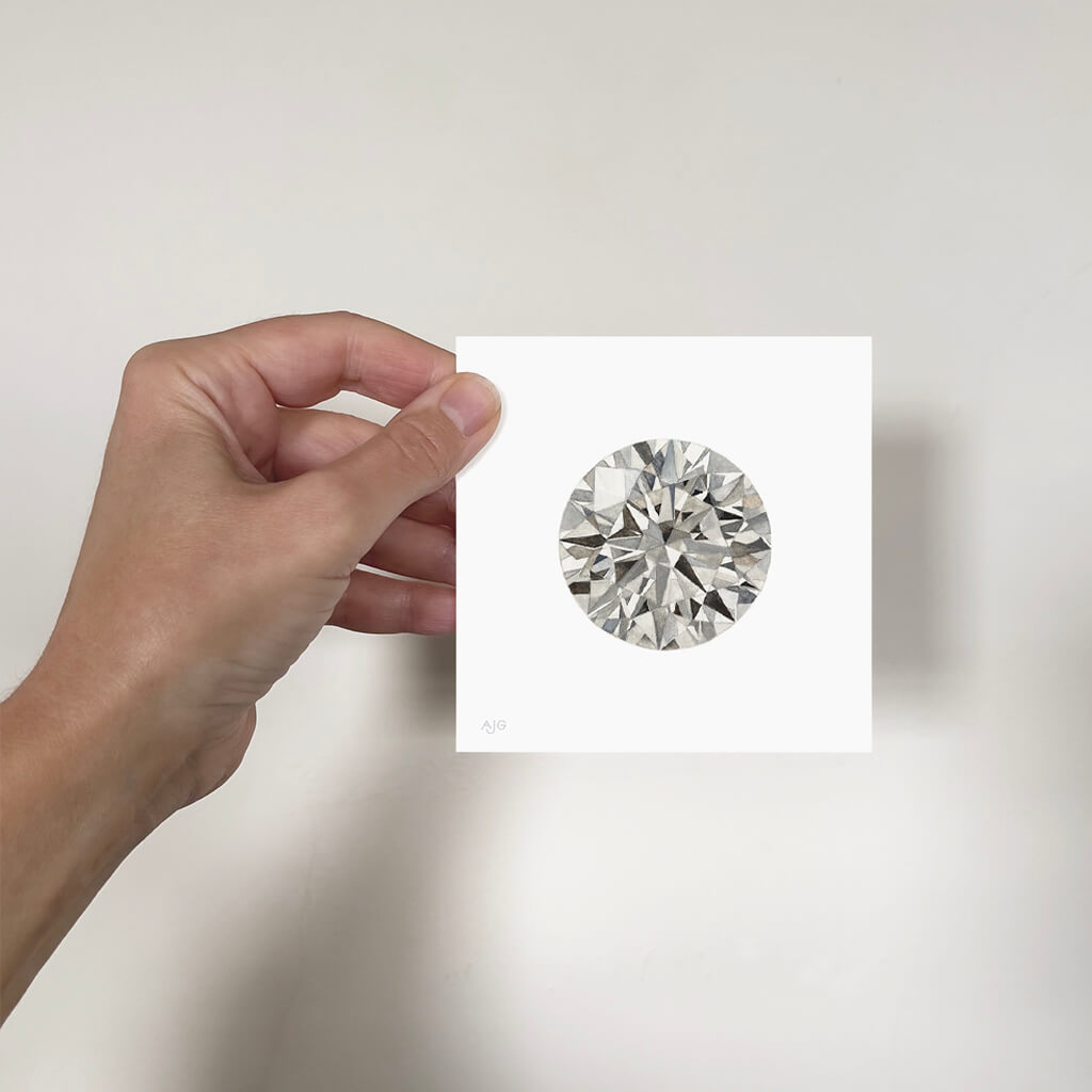 Hand holding a miniature painting of a round diamond against a plain background