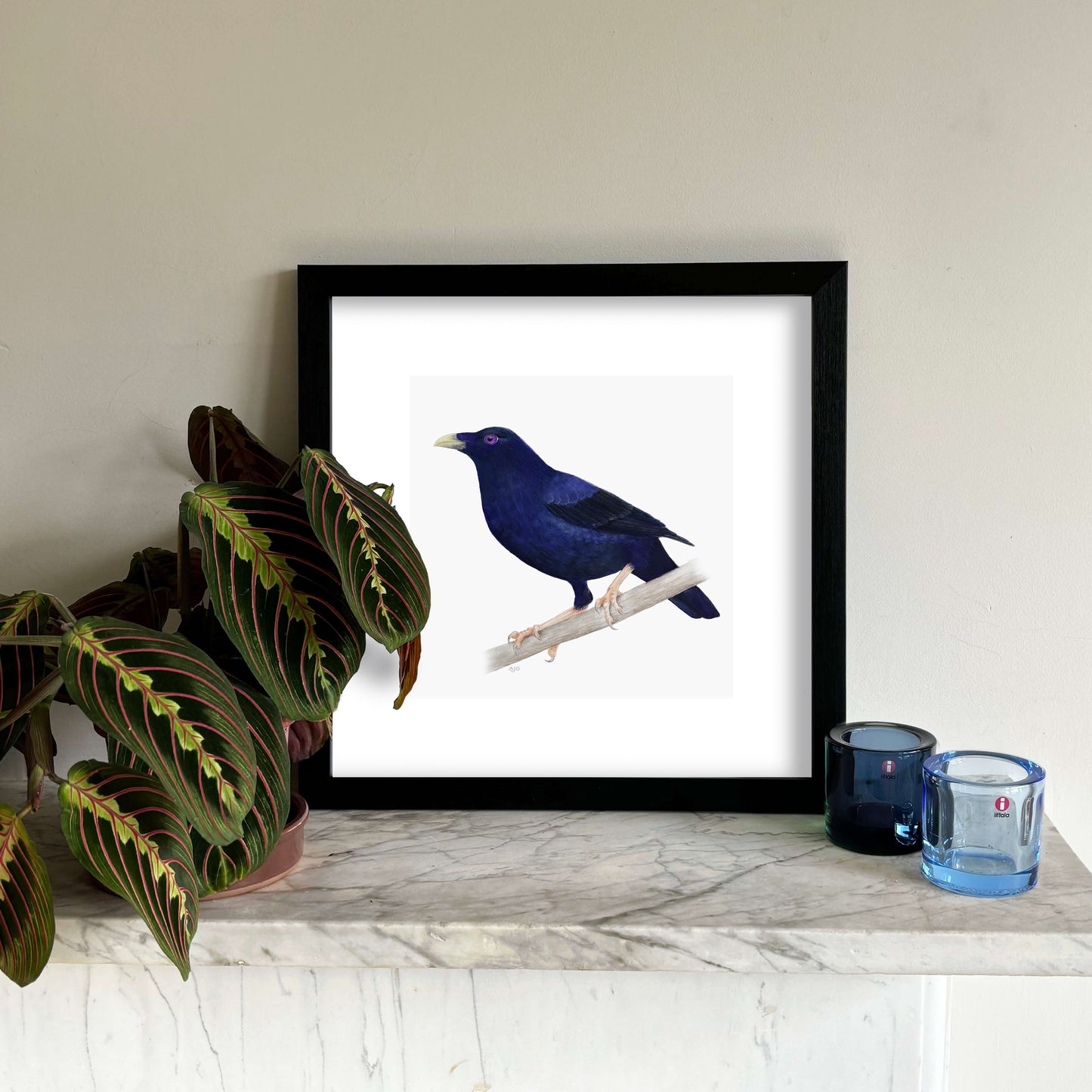 Framed artwork of a blue bird on a white background, placed on a marble surface with decorative items.