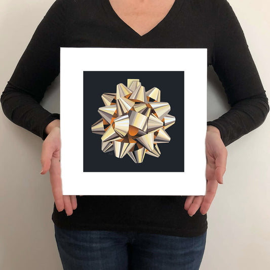 A giclée fine art print on paper of a gold gift bow on a dark charcoal grey background. This image illustrates the print size.