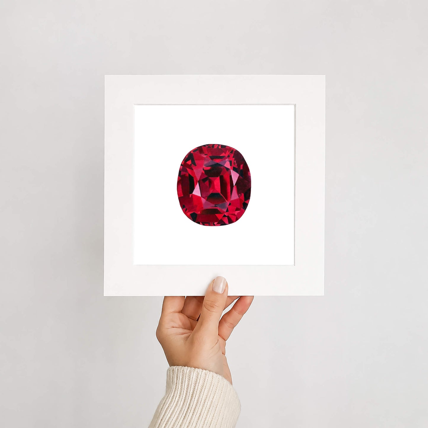 Hand holding a card with a red ruby gemstone illustration against a light gray background