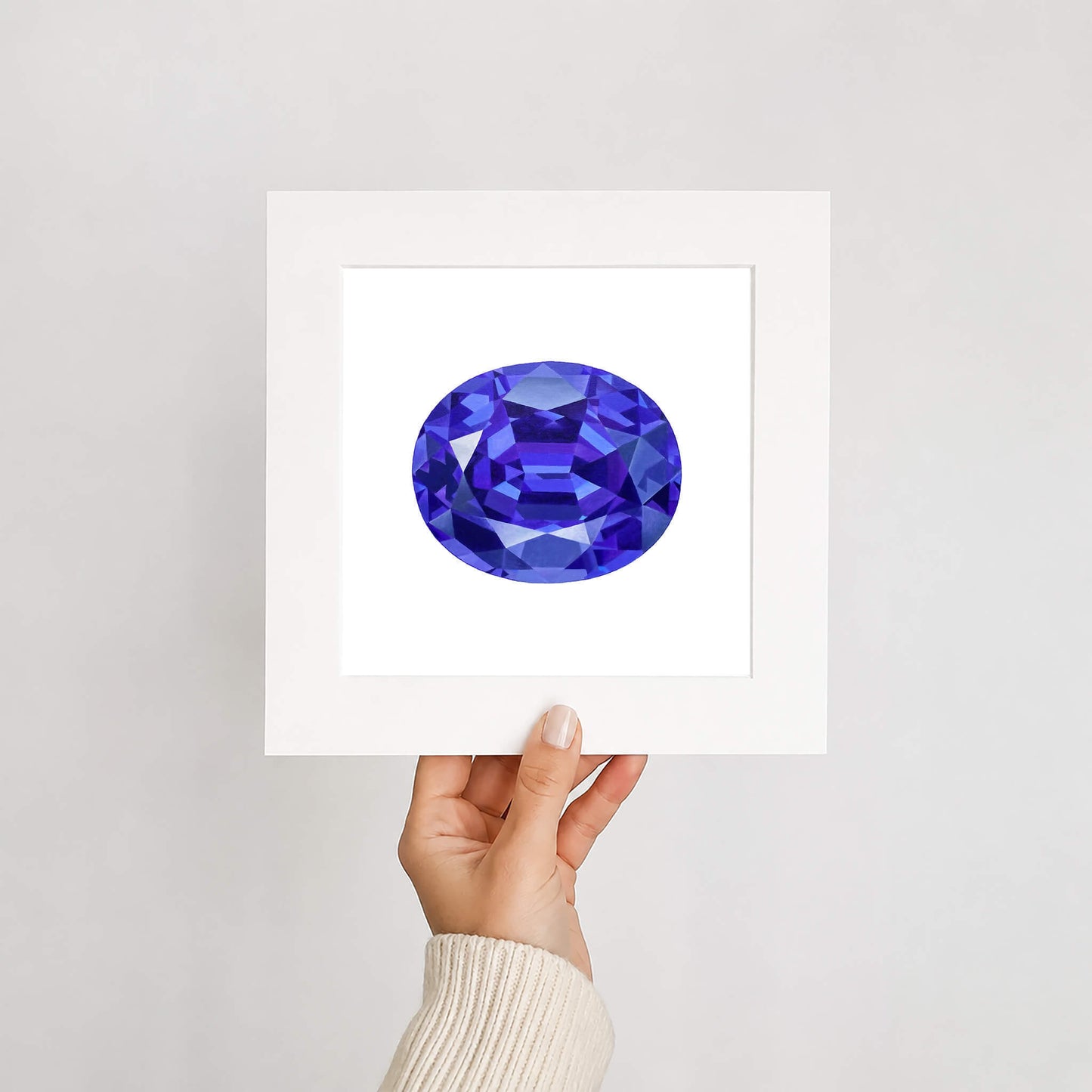 Hand holding an art print of a tanzanite gemstone in white mount on a light gray background