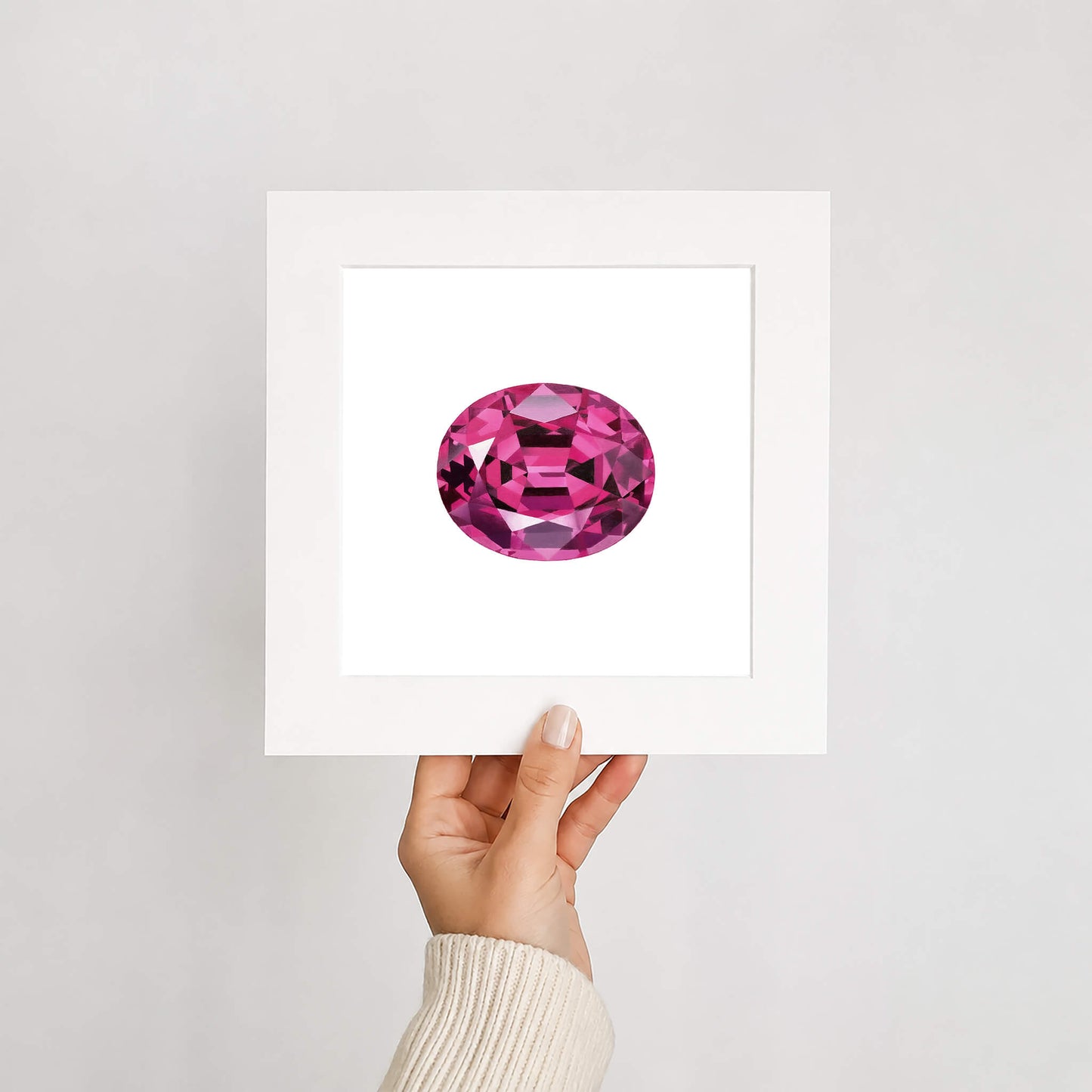 Hand holding a card with a pink gemstone illustration against a white background