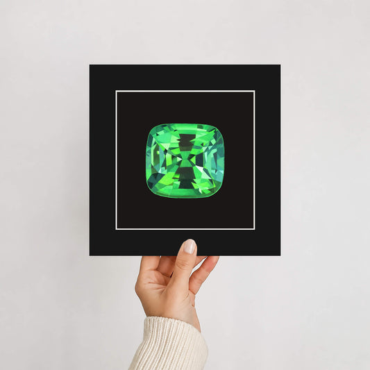 Hand holding a mounted giclée print of a green tsavorite garnet gemstone against a plain background