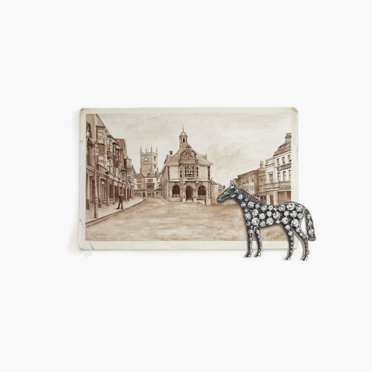 Decorative horse brooch on a sepia-toned illustration of a town square.