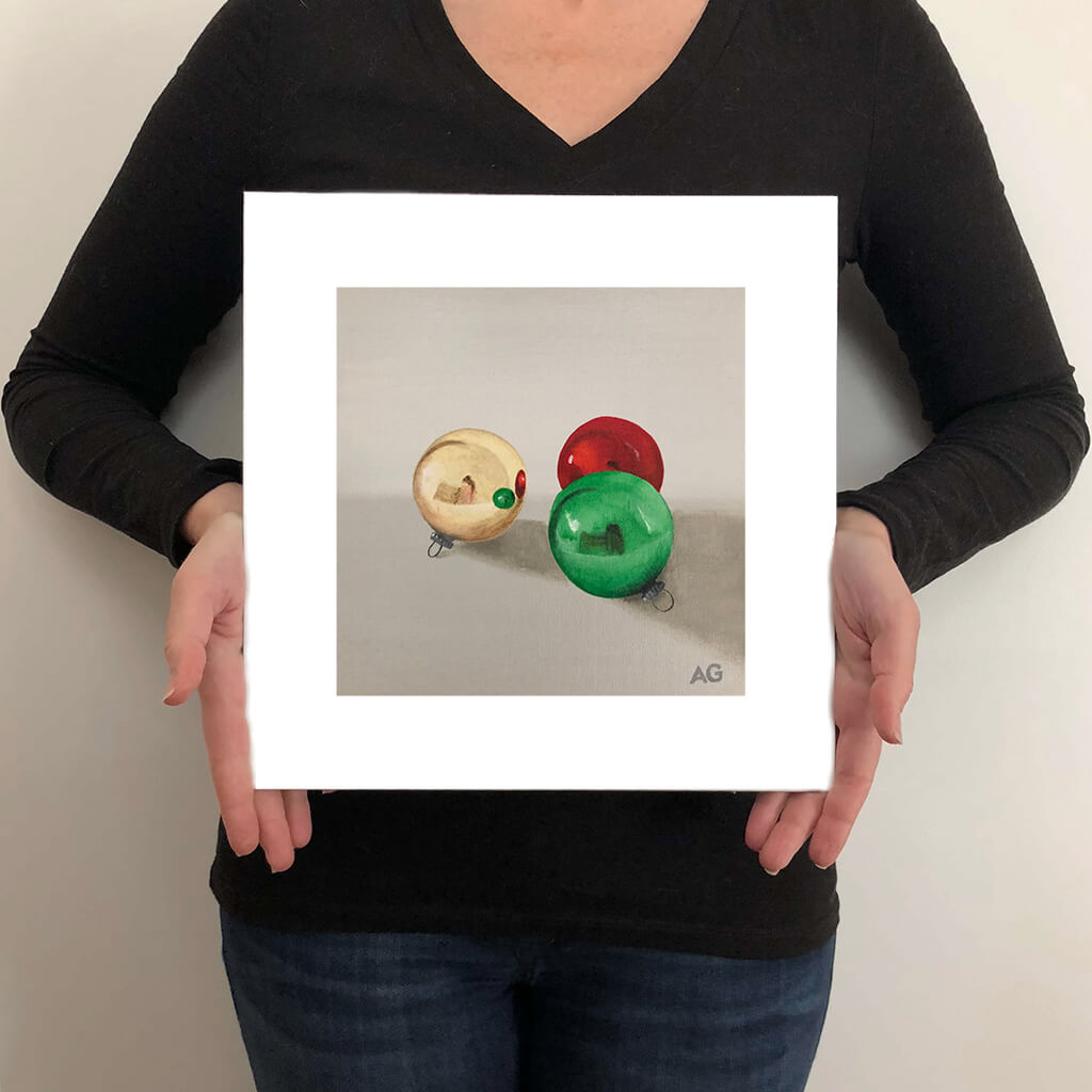 A giclée fine art print on paper of three Christmas tree ornaments on a warm grey background. This image illustrates the print size.
