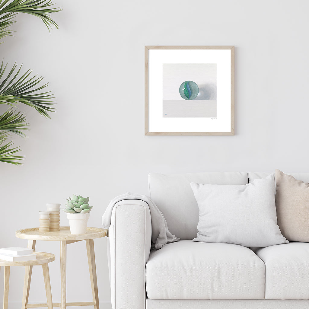 A giclée fine art print on paper of a blue and green glass marble. Image shows the print framed and in a room setting.