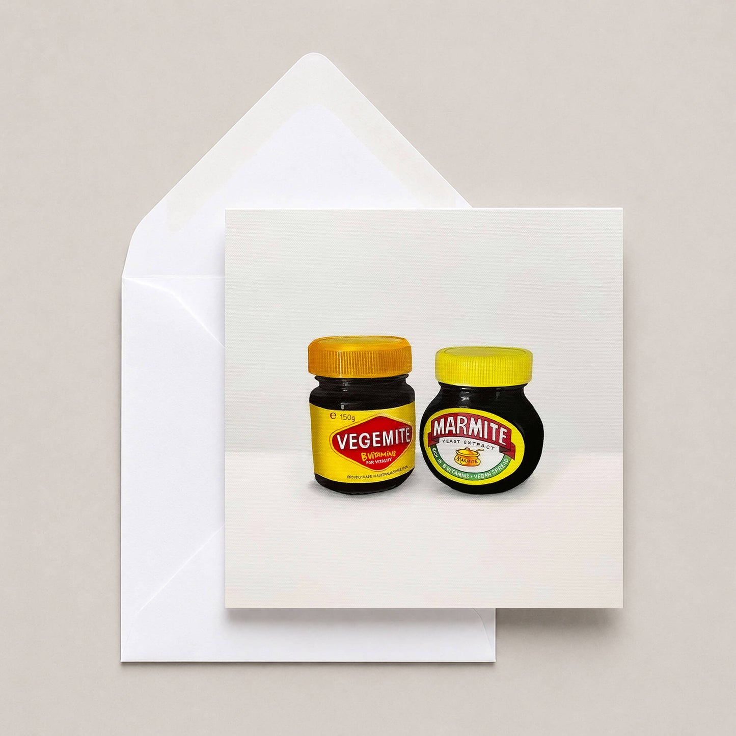 A square greeting card with a white envelope behind it, featuring a printed illustration of two jars: a Vegemite jar on the left and a Marmite jar on the right, against a light neutral background.