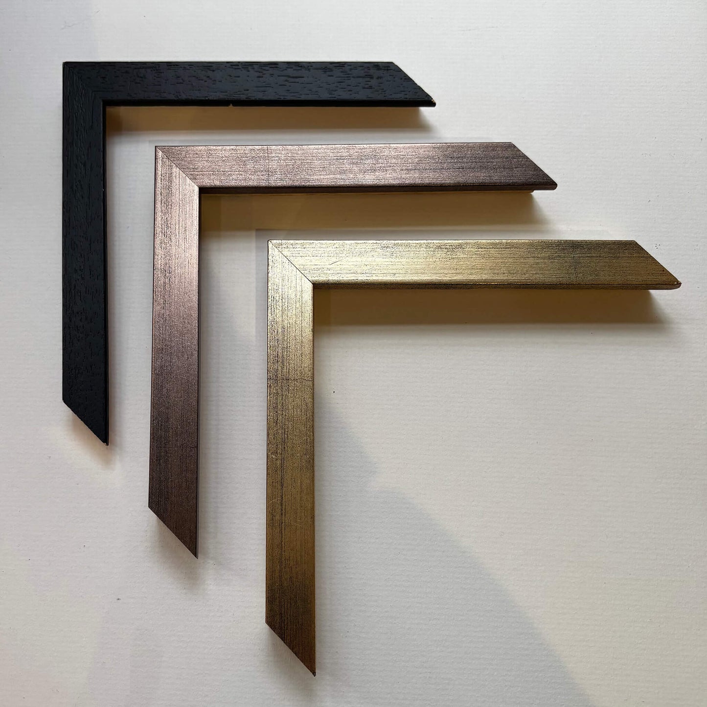 Three picture frame samples in black, bronze, and gold on a grey background