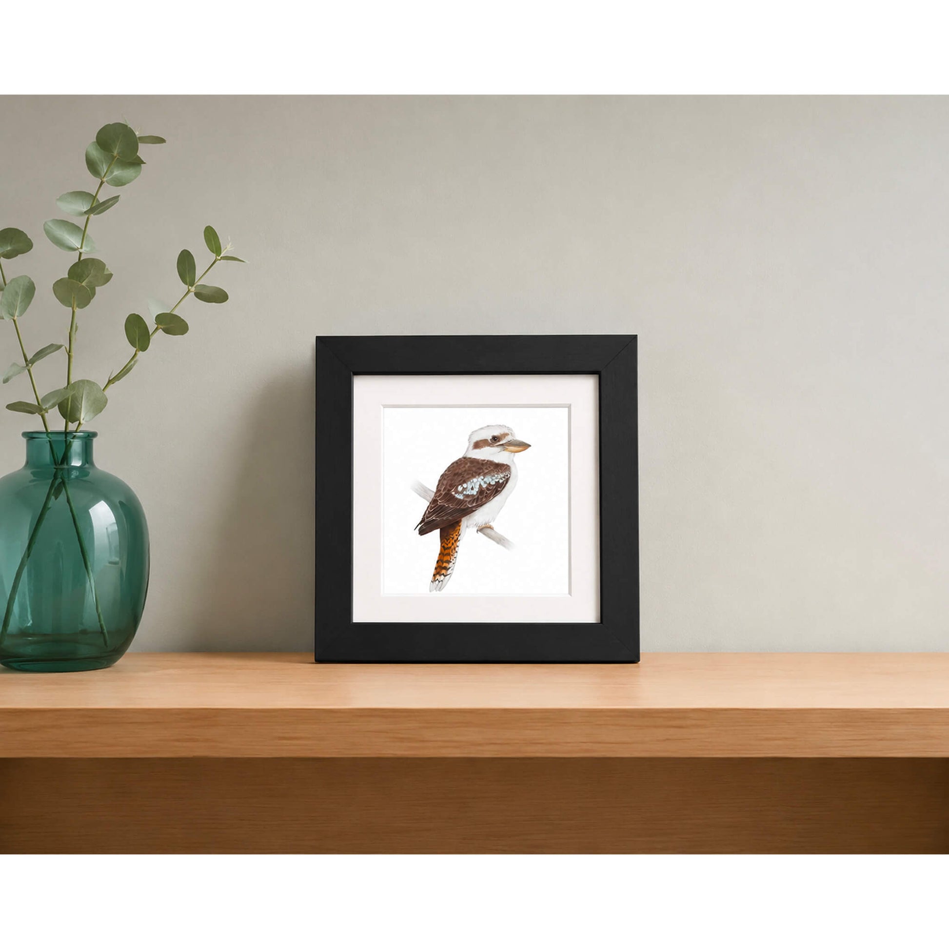 Framed print of a kookaburra on wooden shelf with green glass vase with eucalypt leaves