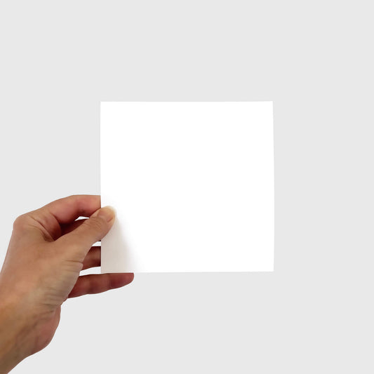 Hand holding a blank square 15cm piece of paper on a light grey background