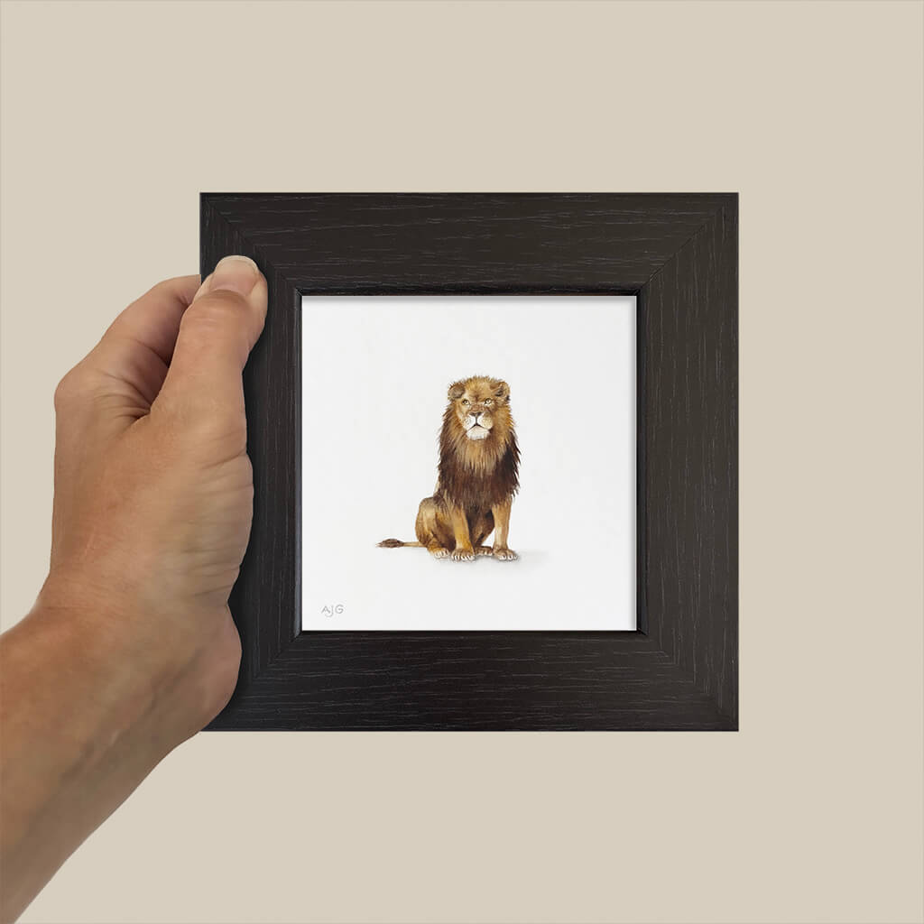 Hand holding a small framed picture of a lion on a beige background