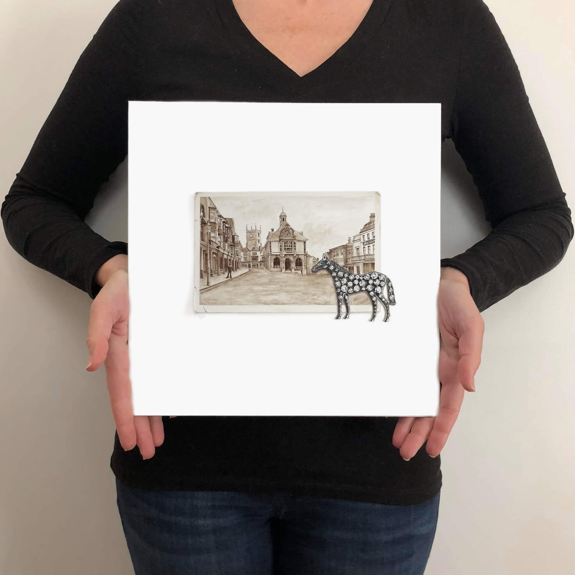 Person holding an unframed painting of a horse brooch and town square scene.