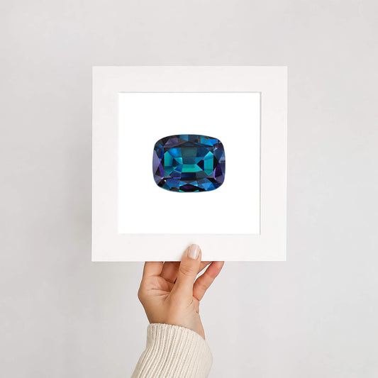 Hand holding a card with a blue gemstone on a light gray background