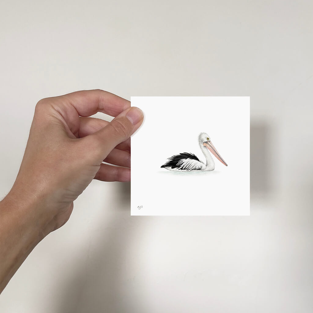 Hand holding a mini painting of a pelican on a plain background