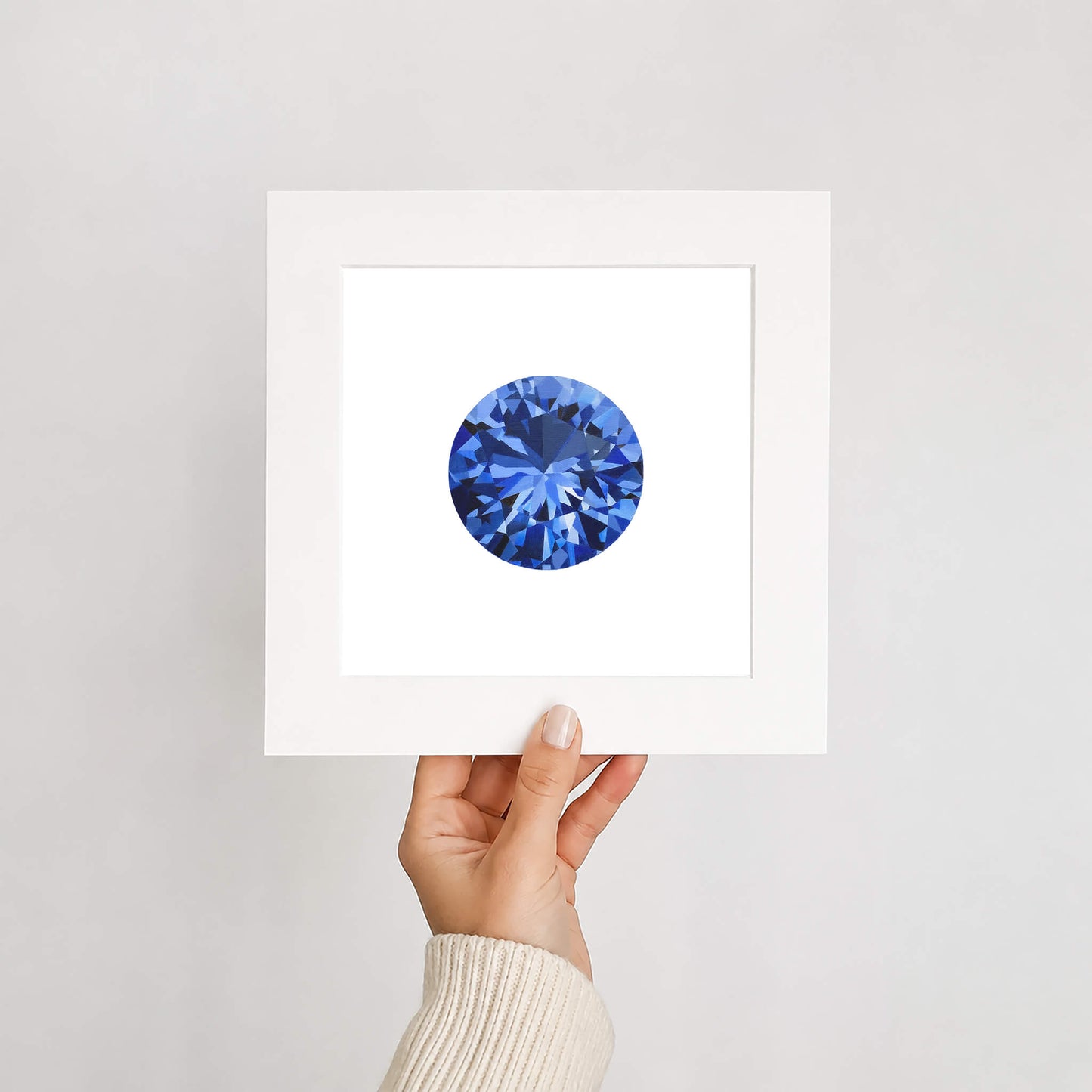 Hand holding a card with a blue gemstone on a light gray background