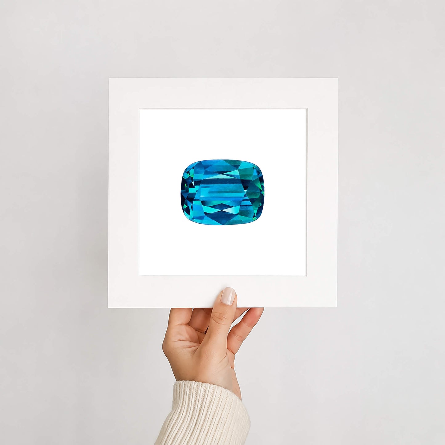 Hand holding a card with a blue gemstone art print on a light gray background