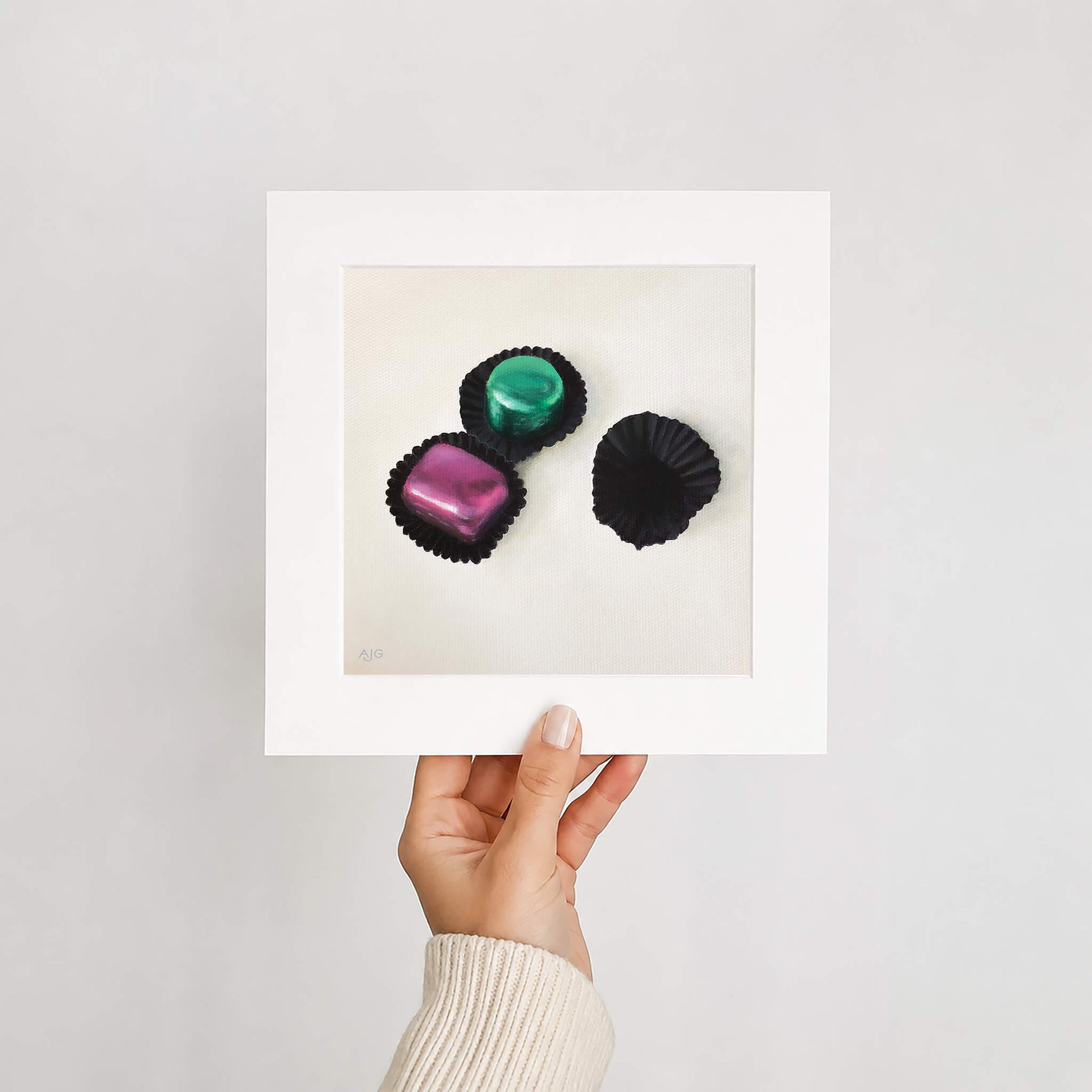 Mounted fine art print of foiled chocolates held by a hand on a white background