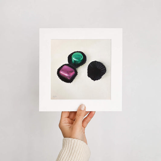 Mounted fine art print of foiled chocolates held by a hand on a white background