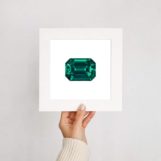 Hand holding a framed emerald gemstone against a light gray background