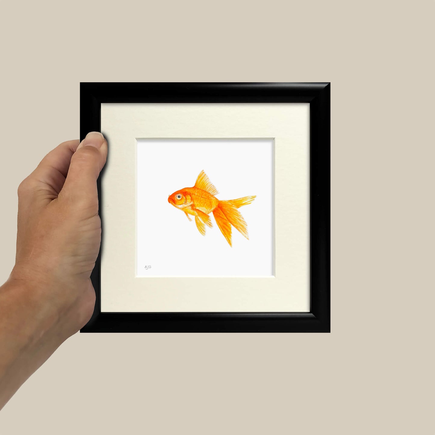 Framed artwork of a goldfish held by a hand against a beige wall.