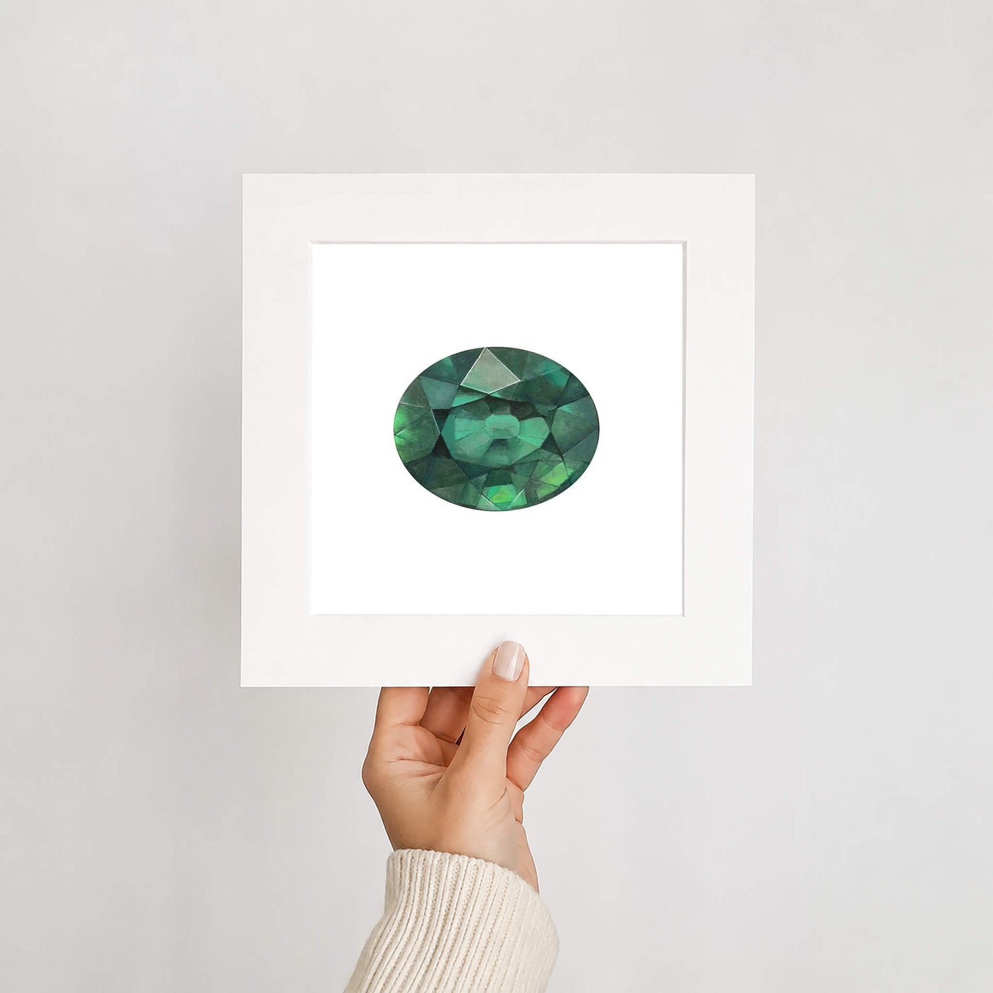Hand holding a card with a green gemstone illustration against a white background