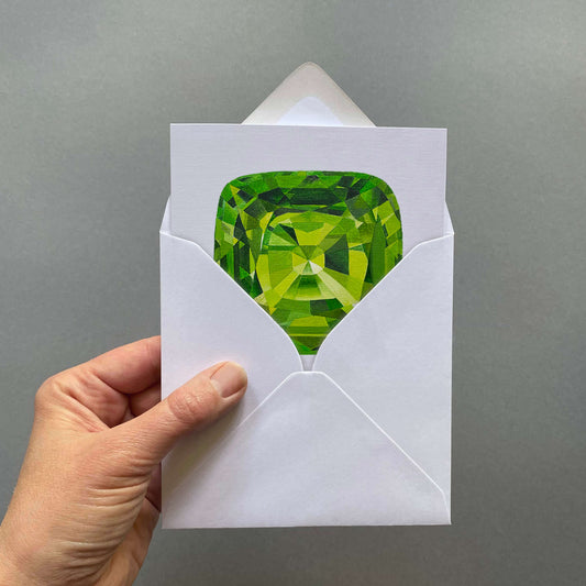 Hand holding a greetings card with a green peridot gemstone design on a pale grey background