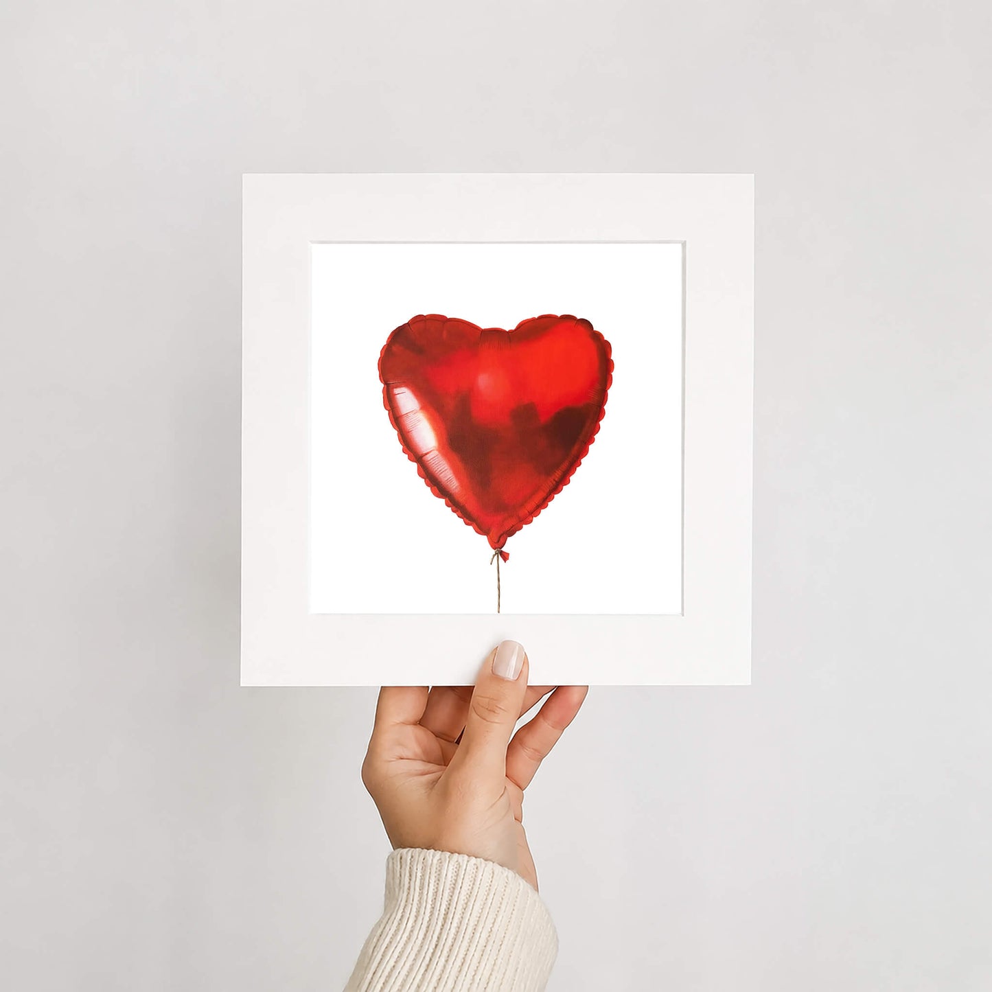 Hand holding a red heart-shaped balloon art print against a white background