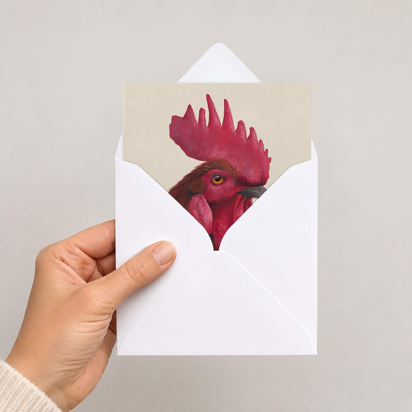 A rooster greetings card in white envelope held by hand