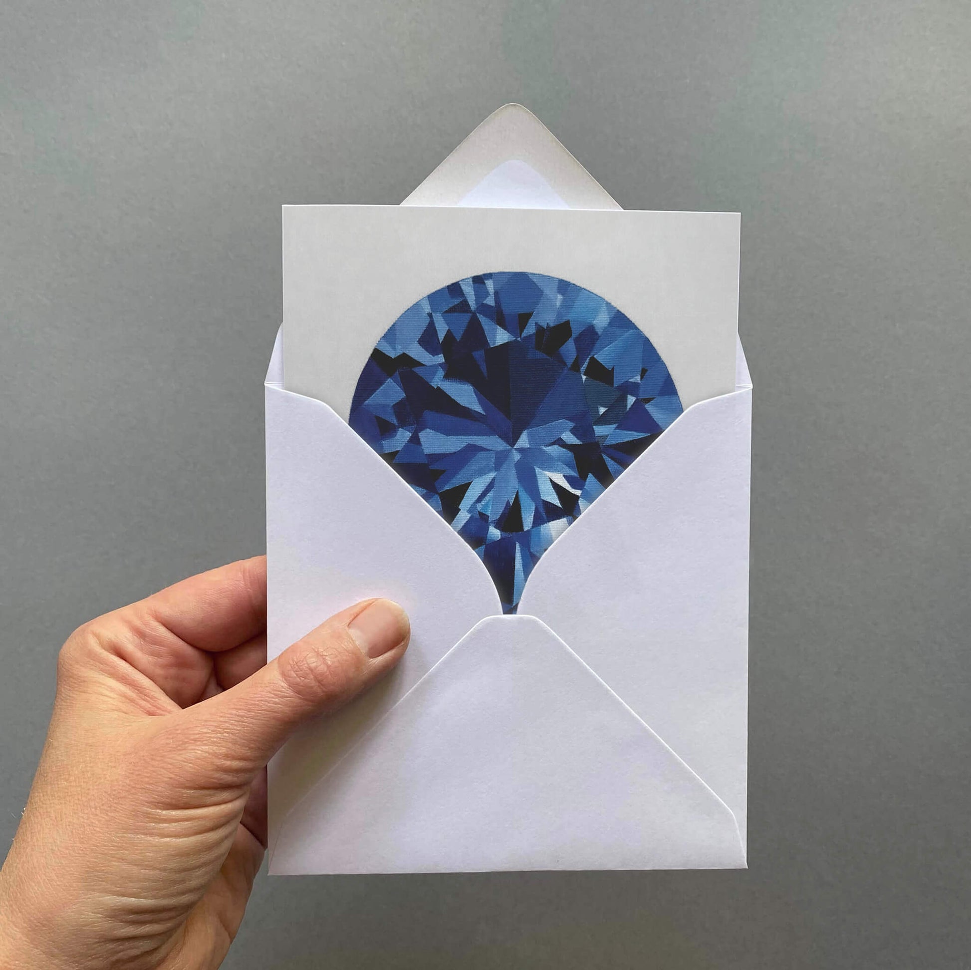 Hand holding a greetings card with a blue sapphire gemstone design on a pale grey background