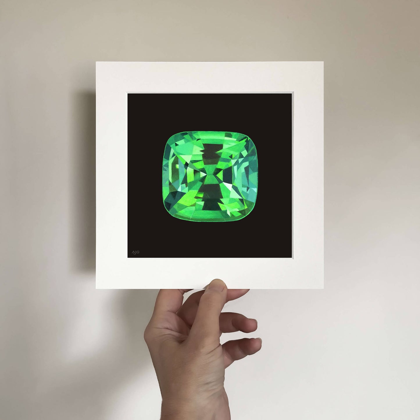 Hand holding a mounted giclée print of a green tsavorite garnet gemstone against a plain background