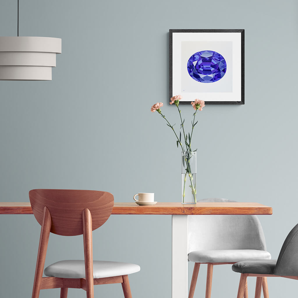 A gemstone giclée fine art print on paper of a tanzanite on a light grey background. Image shows the print framed and in a room setting.